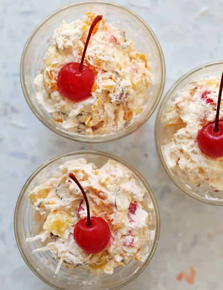 creamy ambrosia fruit salad in three small cups with a cherry on top