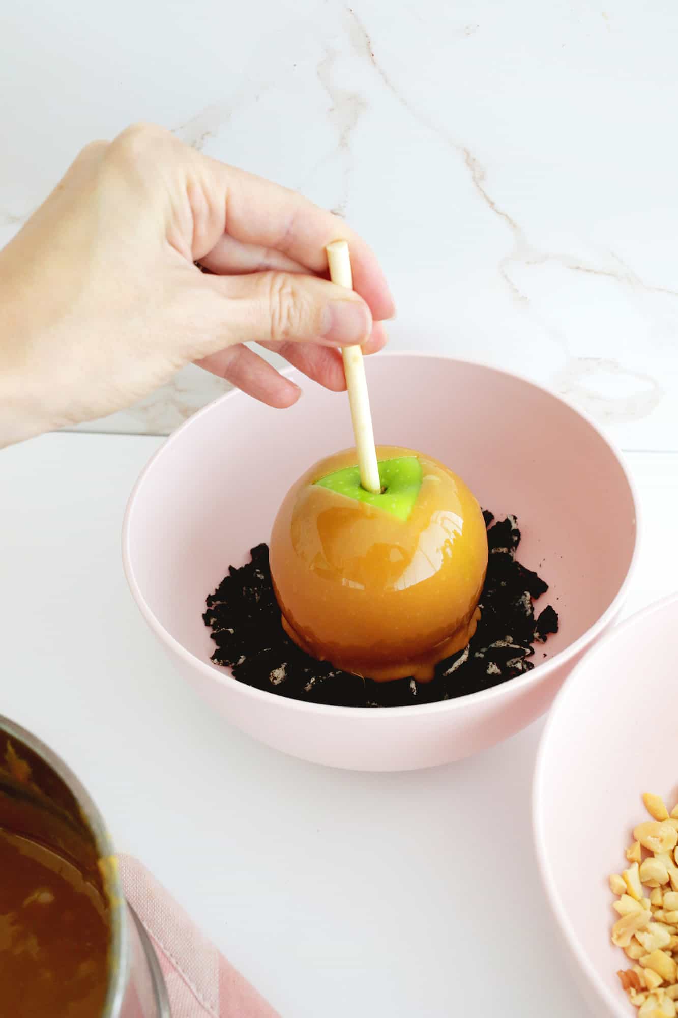 Caramel apple being dipped into crushed oreo