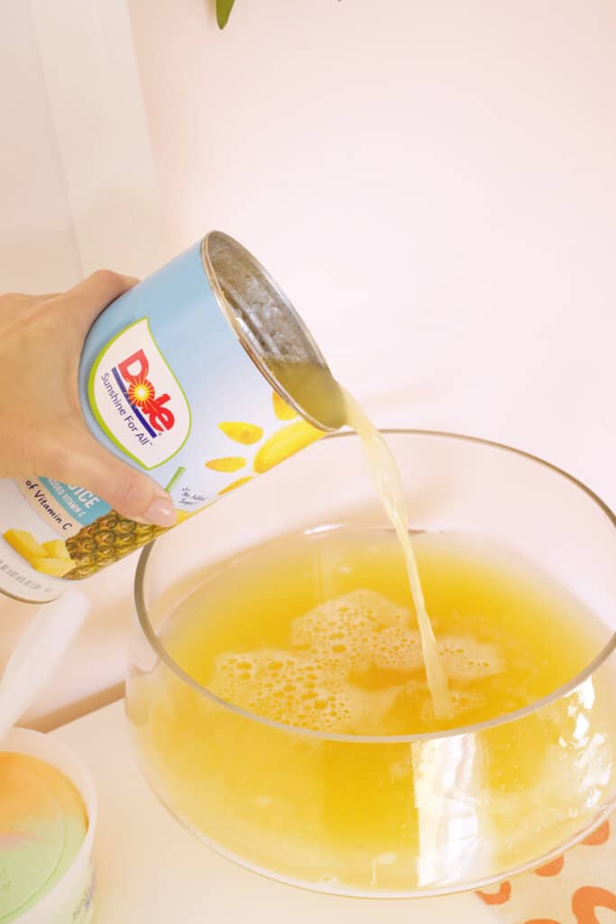 pouring pineapple juice into rainbow sherbet punch