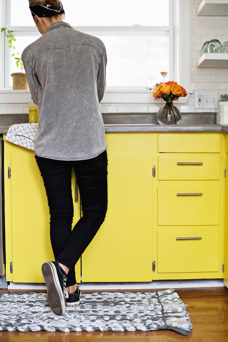 someone standing in kitchen with yellow cabinets on the woven rag rug