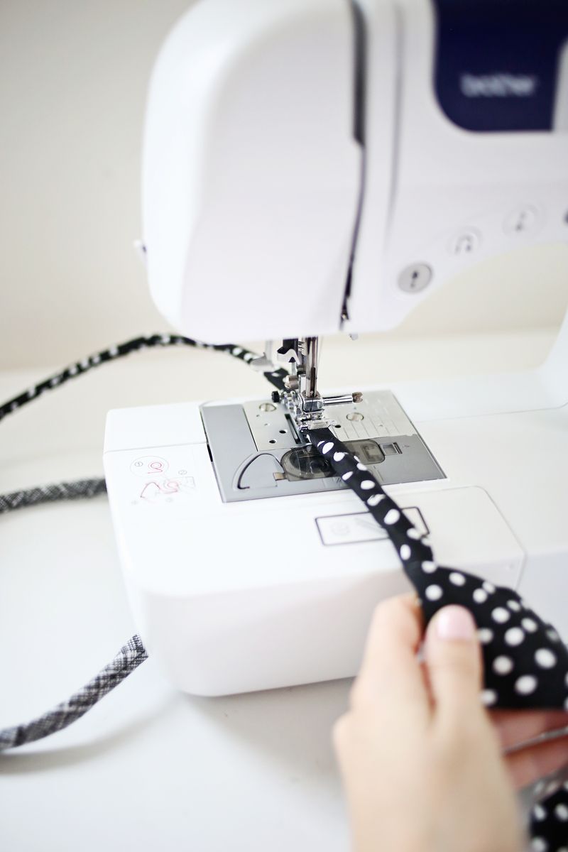 a black with white polka dots strip of fabric rolled up and being sewn together in a sewing machine 