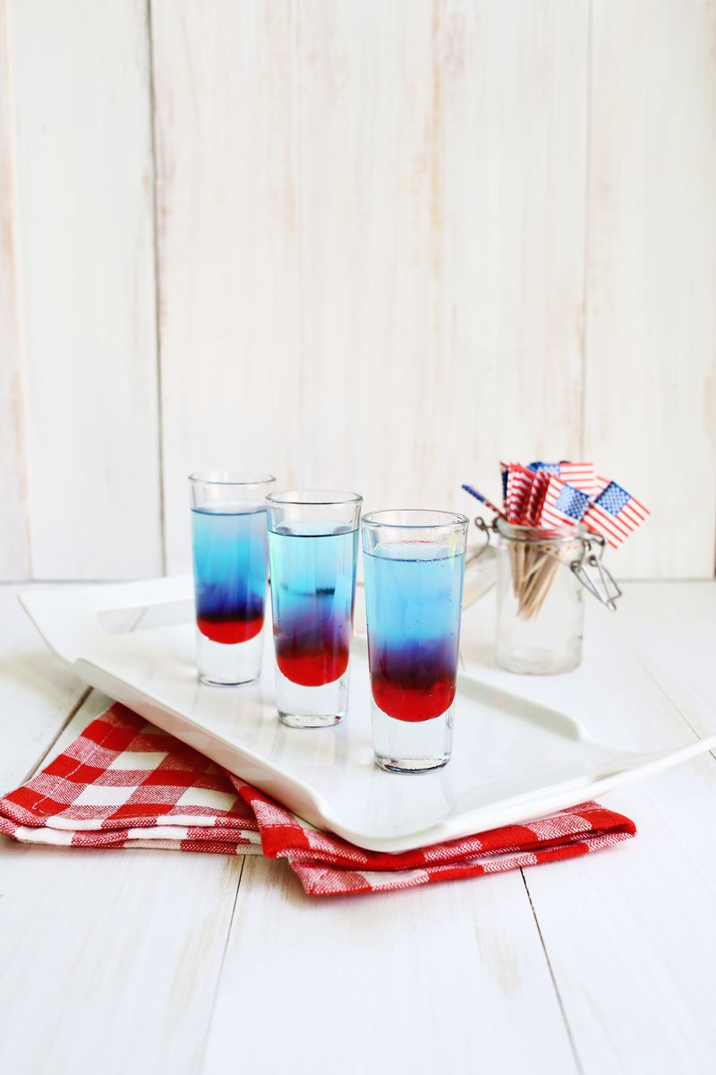 3 glasses of bomb pop shots on a white platter with a jar full of American flags next to it
