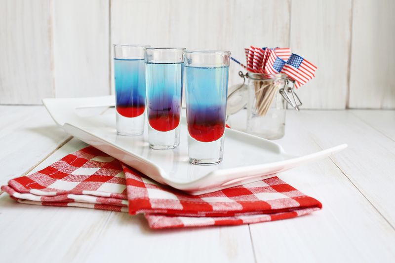 3 glasses of bomb pop shots on a white platter with a jar of American flags next to it
