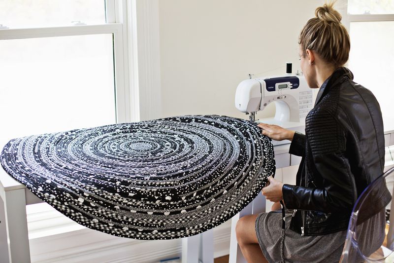 Someone sewing the round black and gray rug in a sewing machine