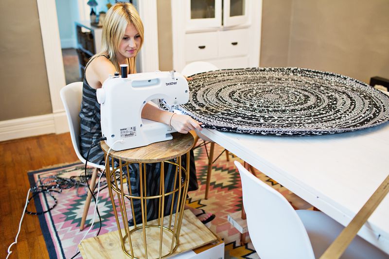 a blonde woman sewing the round black and gray rope rug with a sewing machine