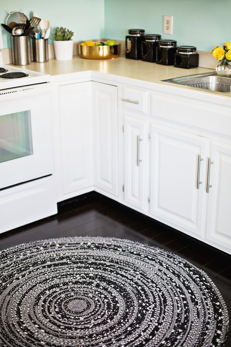 a teal kitchen with white cabinets and a tan countertops with a black and gray circle rope rug on a black floor