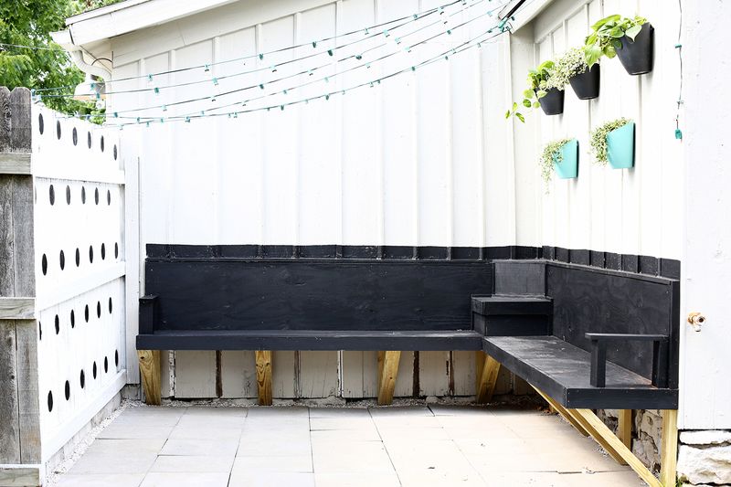 a black bench with no seat cushion or pillows on it on a deck with string lights hanging over it