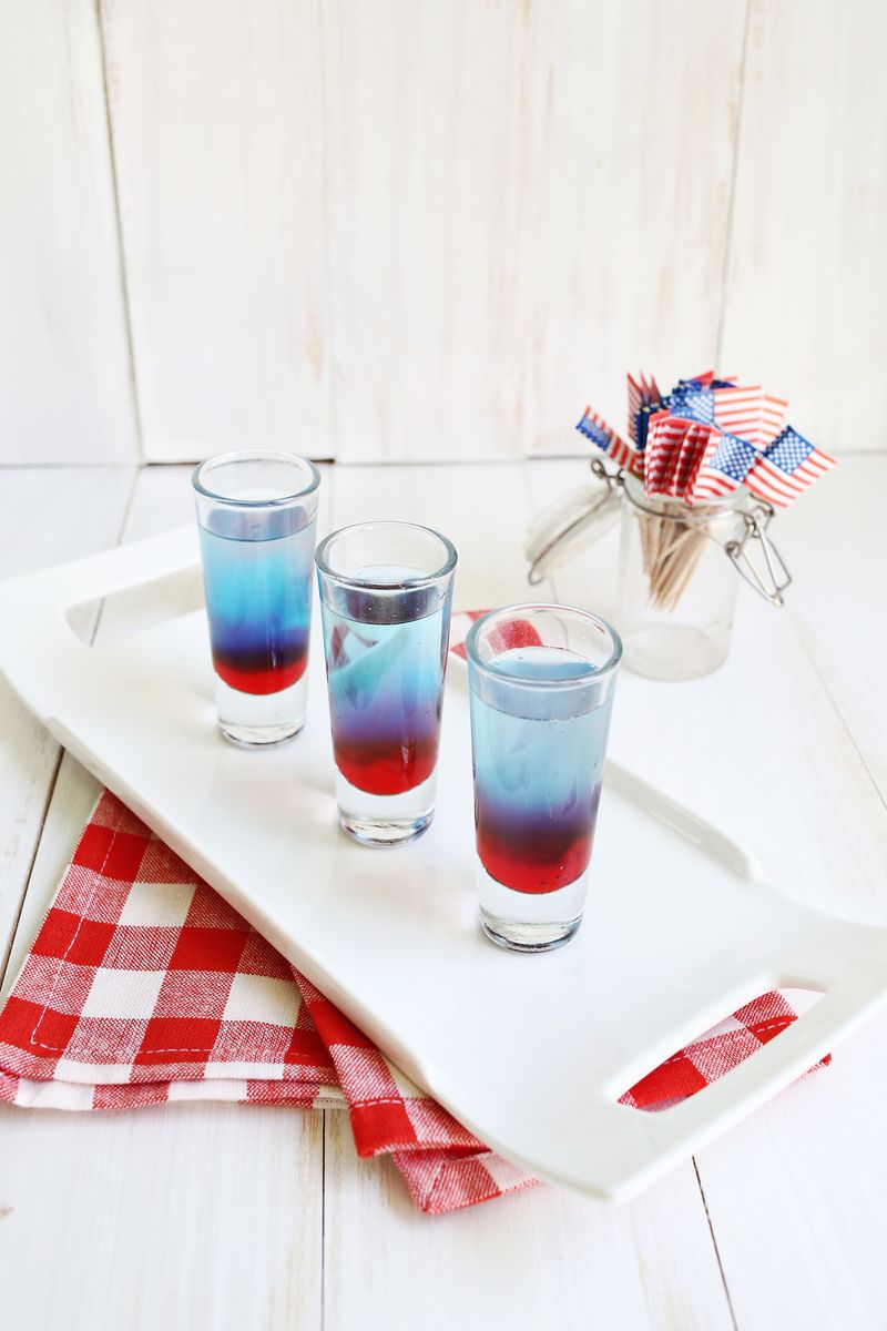 3 glasses of bomb pop shots on a white platter with a jar of American flags next to it