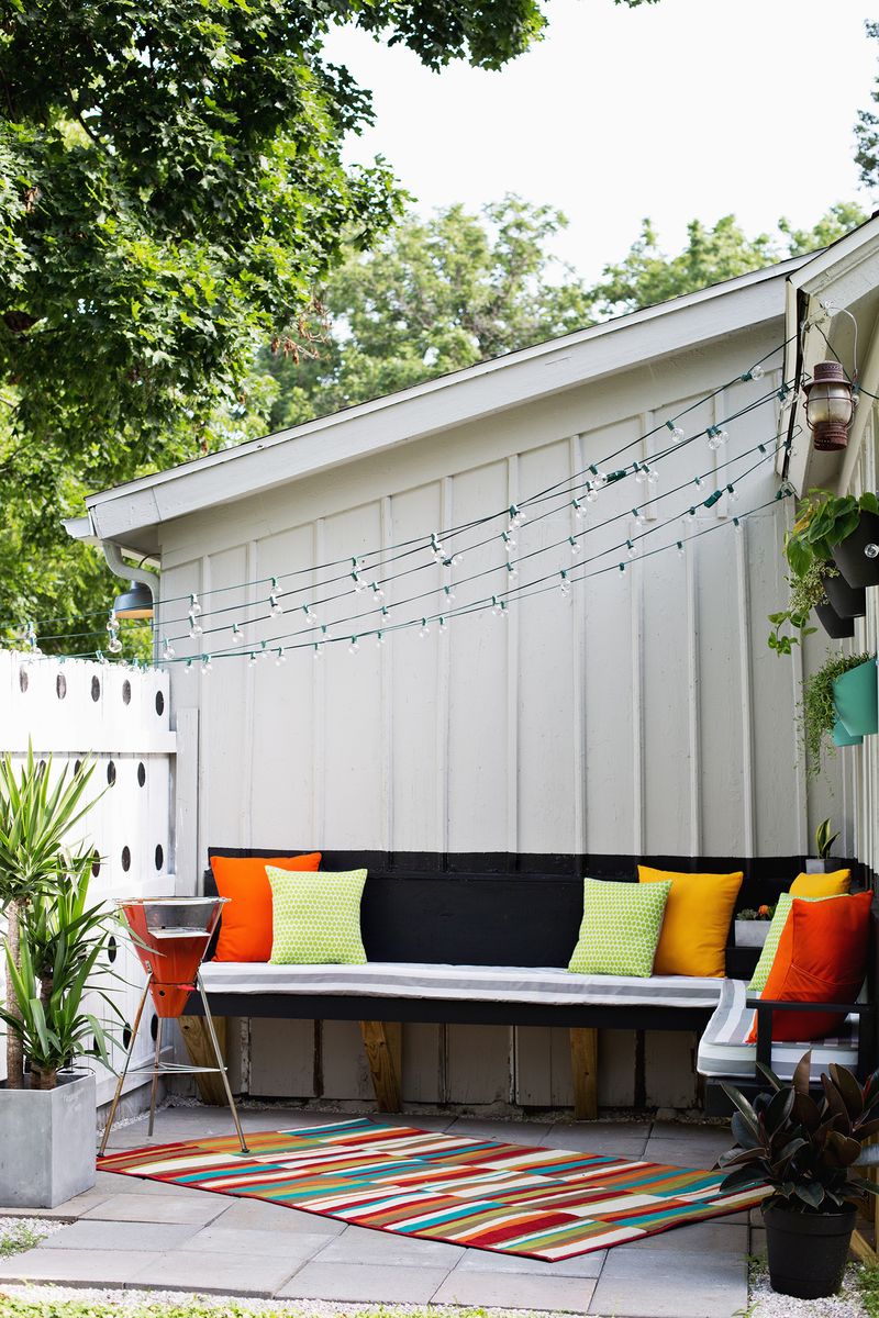 a black bench with a white and gray stripped seat cushion on a deck with string lights above it