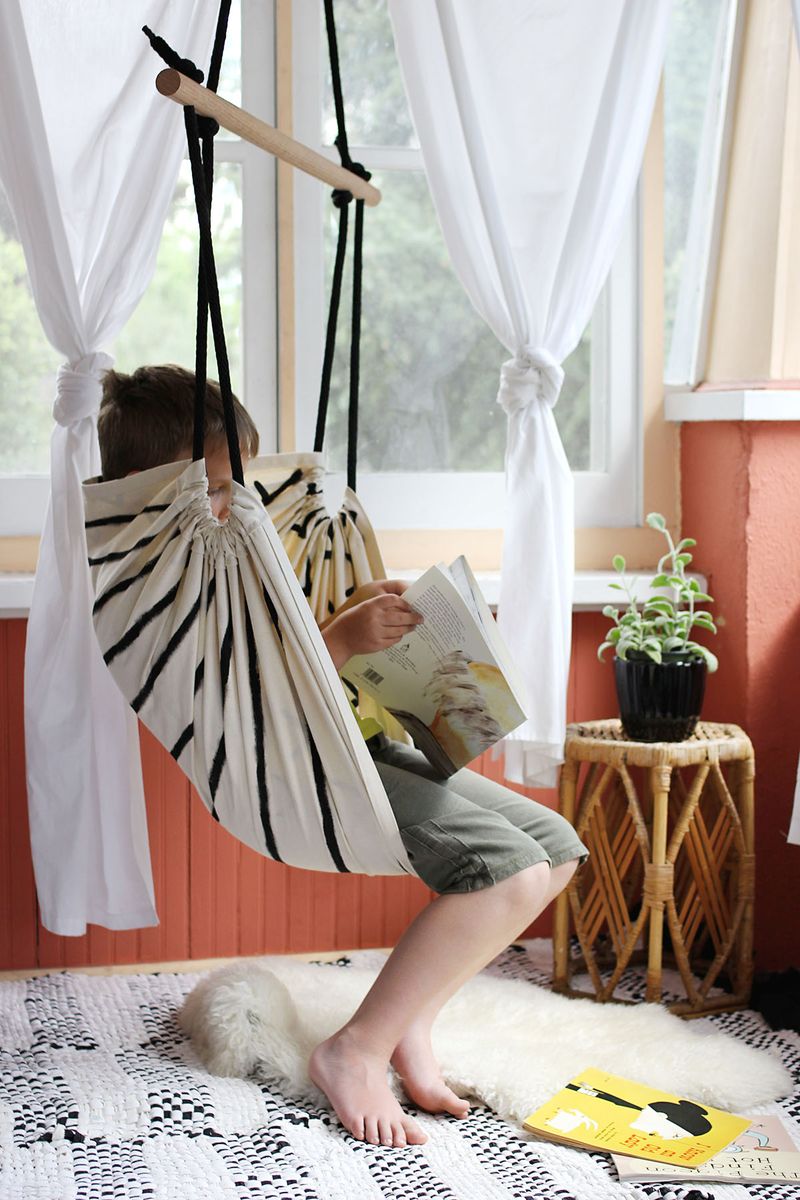 a boy sitting in a hammock chair reading a book