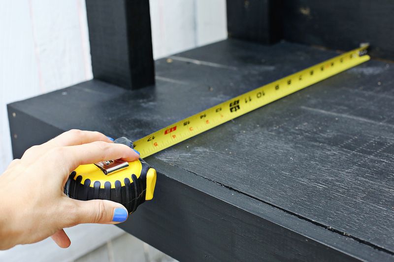 someone using a tape measure to measure the seat of a black bench
