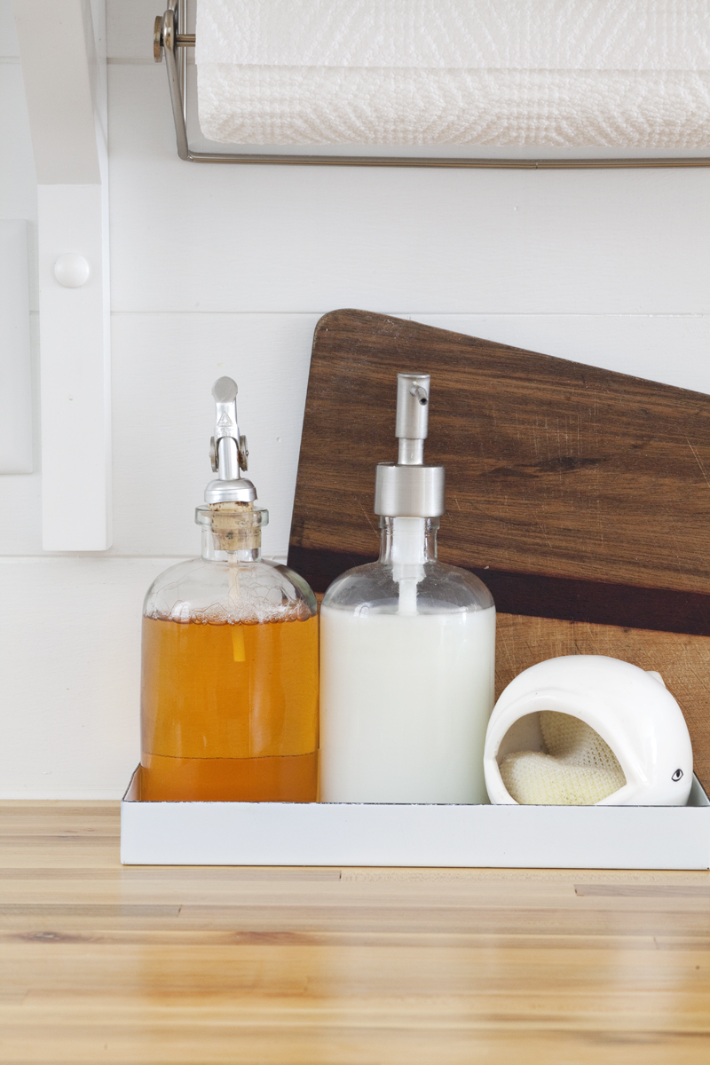 close up of butcher block countertop with a glass bottle of dish soap, hand soap, and a sponge on it