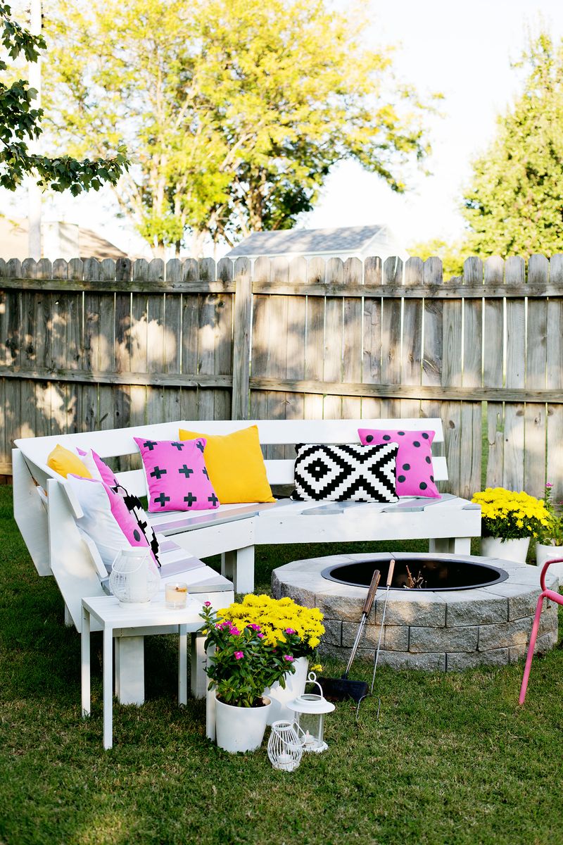 Backyard with a bench with pillows around a firepit and some potted flowers