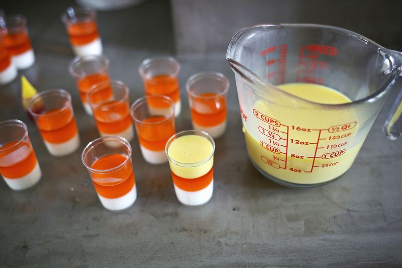 a mixing cup with milk mixture in it and 12 shot glasses next to it