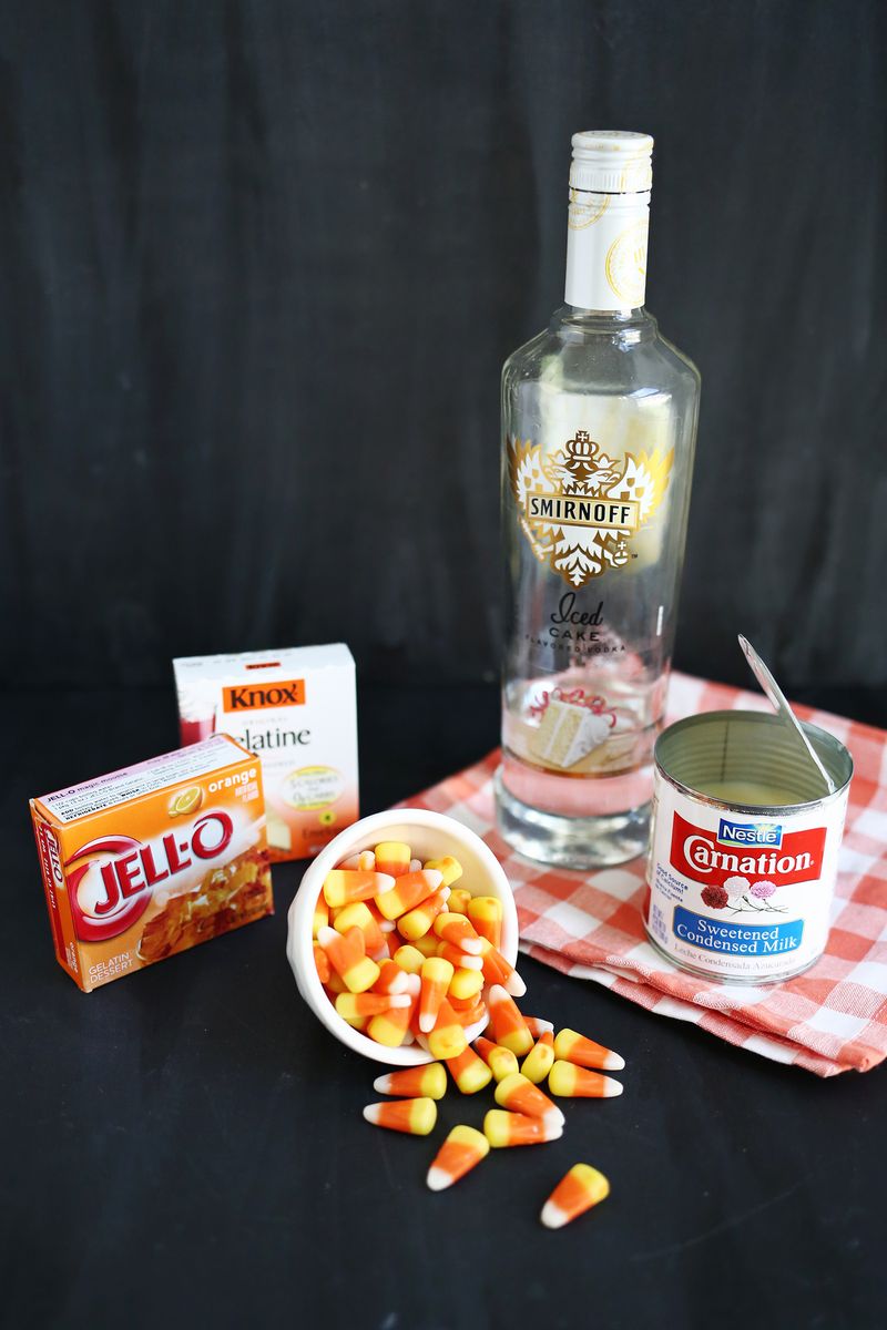 a bottle of smirnoff, a box of jell-o, a box of gelatine, a bowl of candy corn, and a can of condensed milk 