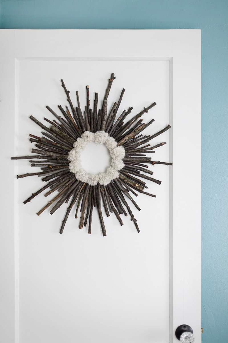 twig pom pom wreath on a white door in front of a teal wall