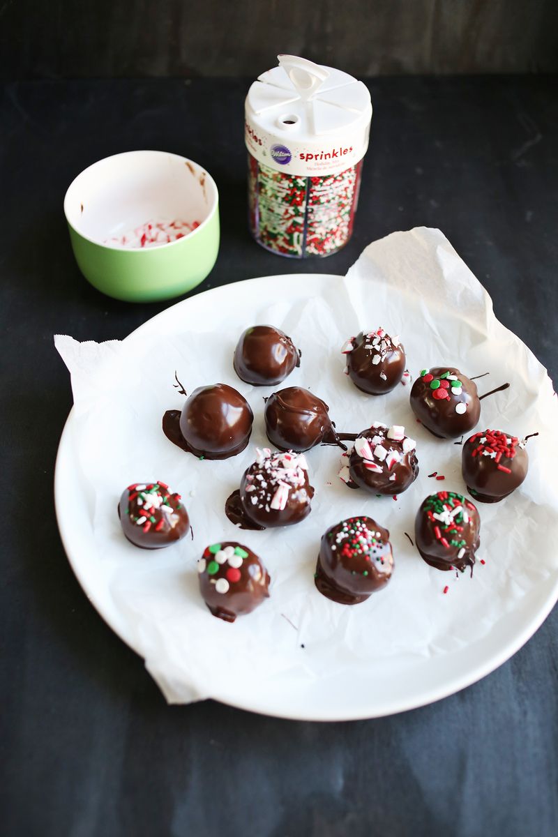 oreo truffles with sprinkles on them on a white plate with a bowl and can of sprinkles next to it