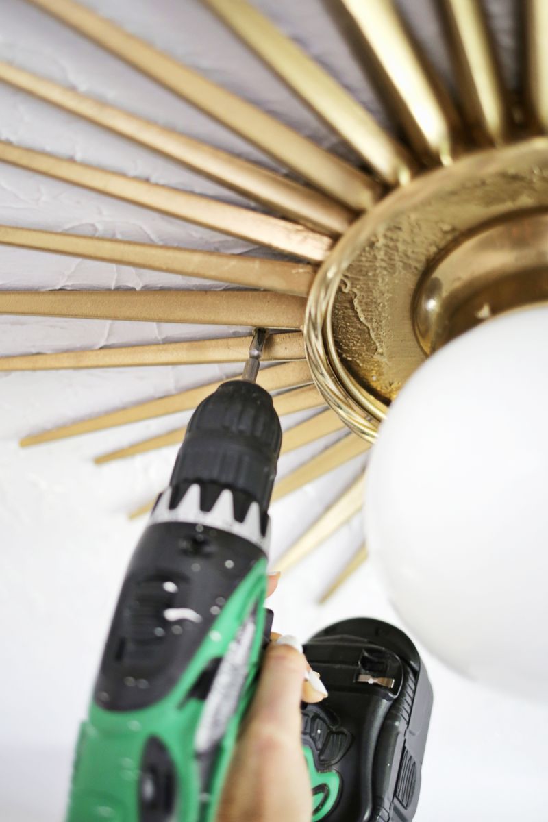 someone drilling into the ceiling to secure the gold sunburst mirror medalion around the light fixture