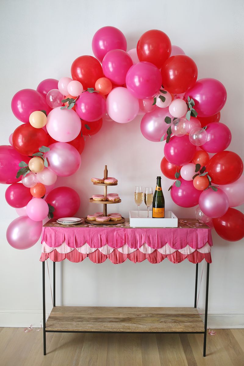 a pink and red balloon arch over a table with cookies and drinks on it 