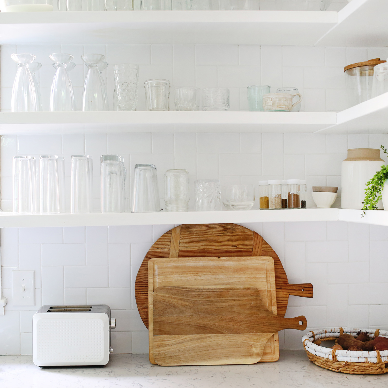white shelves with clear glasses on it and a toaster and wooden cutting boards on countertop