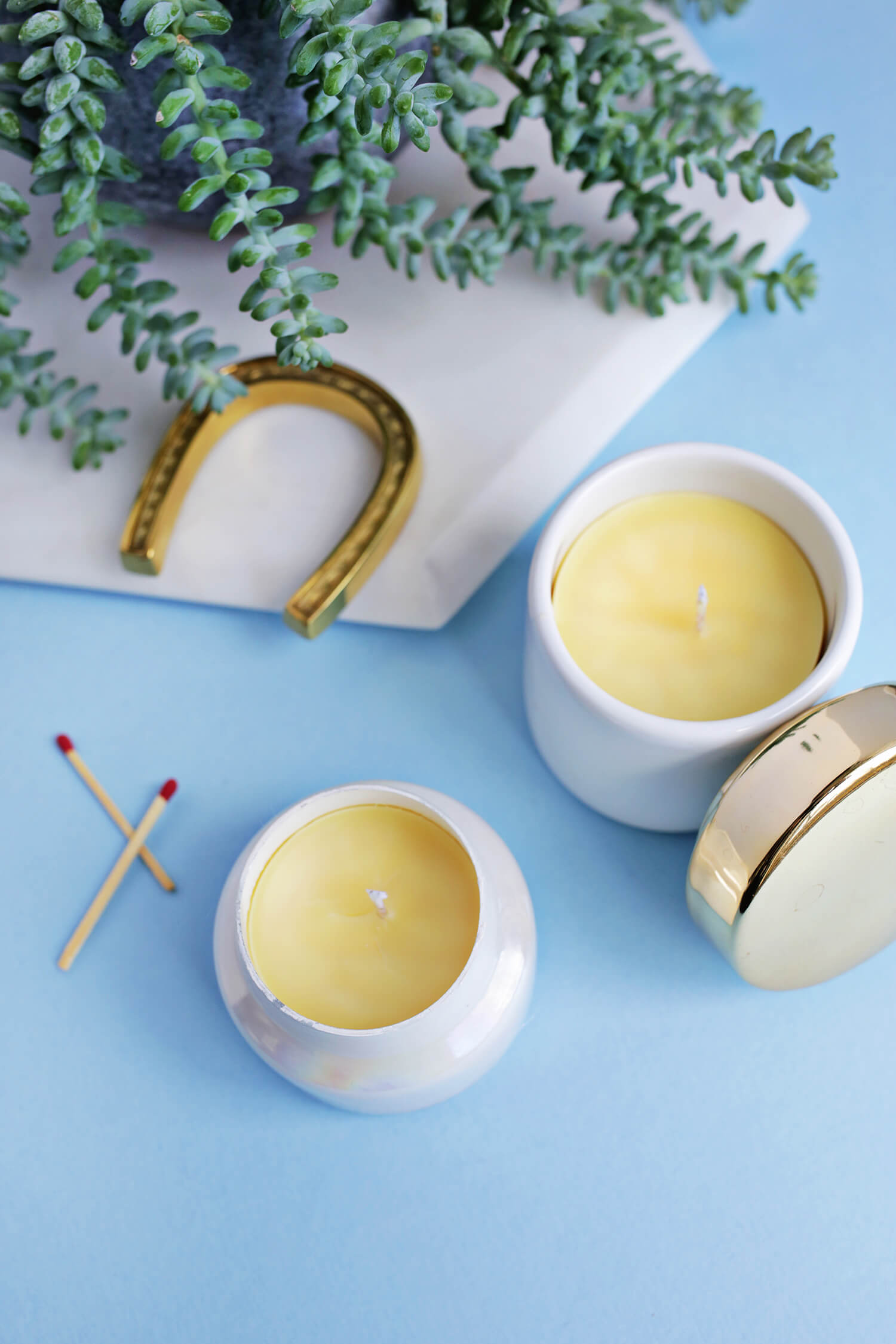 2 beeswax candles with 2 matches, a plant, and a gold horseshoe next to them