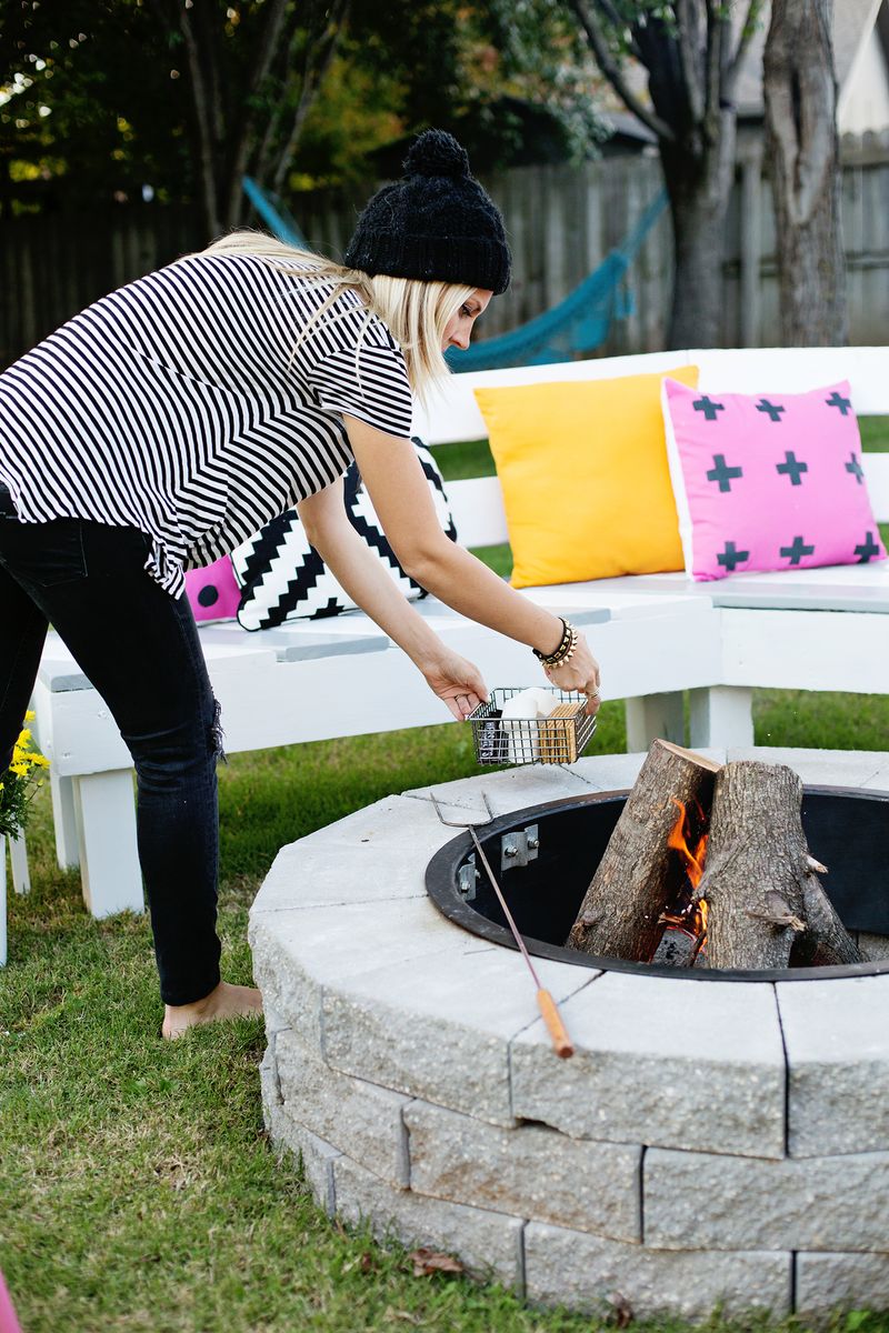 a woman holding a smores basket by the firepit with a fire going and the marshmallow skewer on it