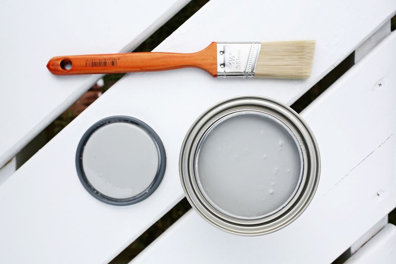 a can of gray paint with the lid off and a paintbrush