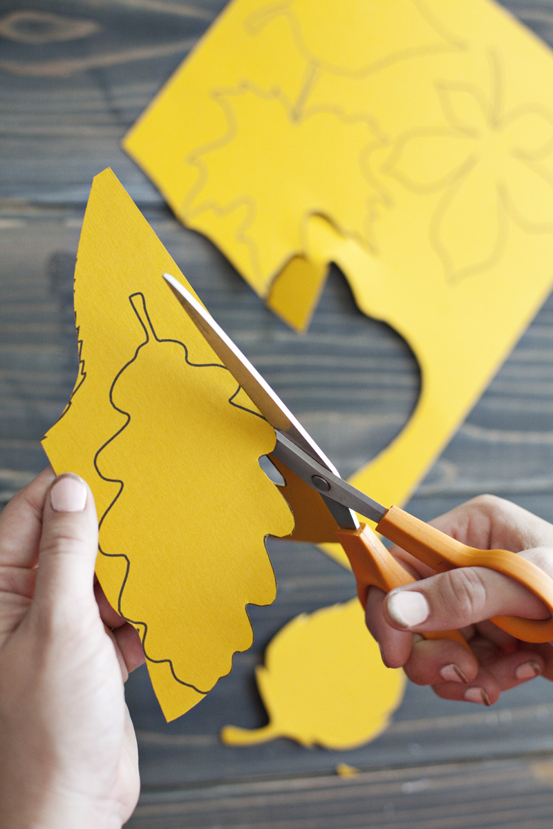 someone cutting out the leaf designs on yellow construction paper