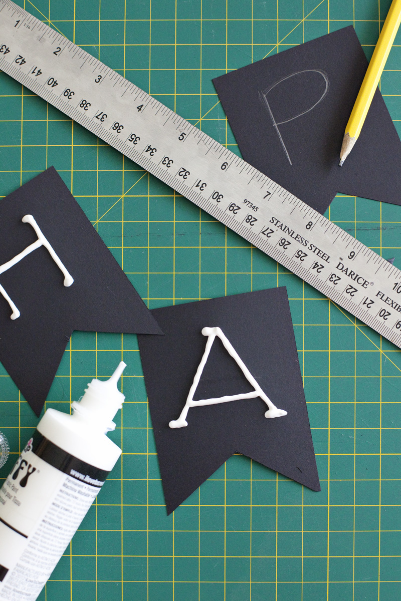 3 cut out black construction paper with the letters H, A, and P on them in puffy paint and a ruler and pencil on top