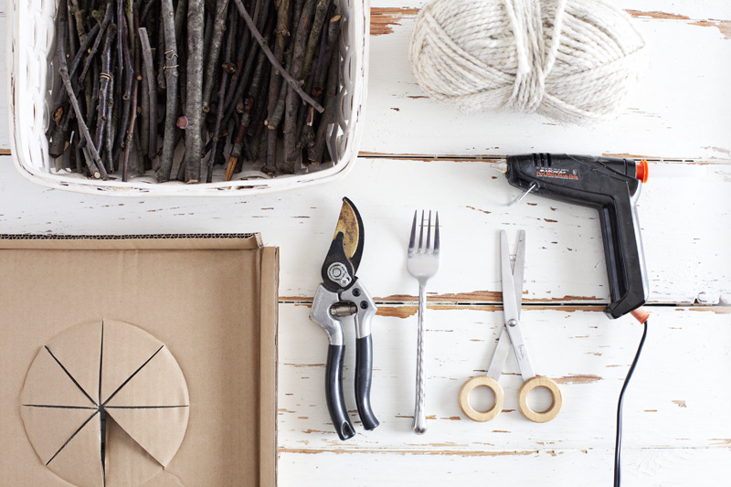 a basket of twigs, a ball of white yarn, a cardboard box, forkl, scissors, hot glue gun, and trimmer