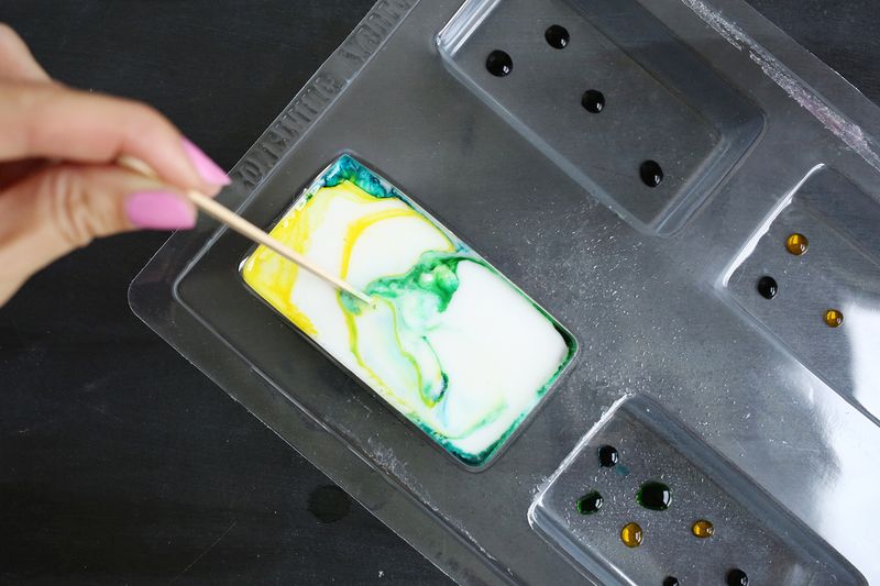 someone using a toothpick to spread soap dye in soap mold