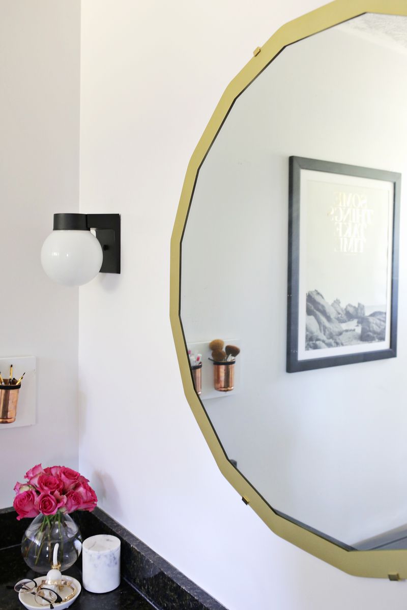 a gold framed circle mirror over a bathroom sink with black countertop