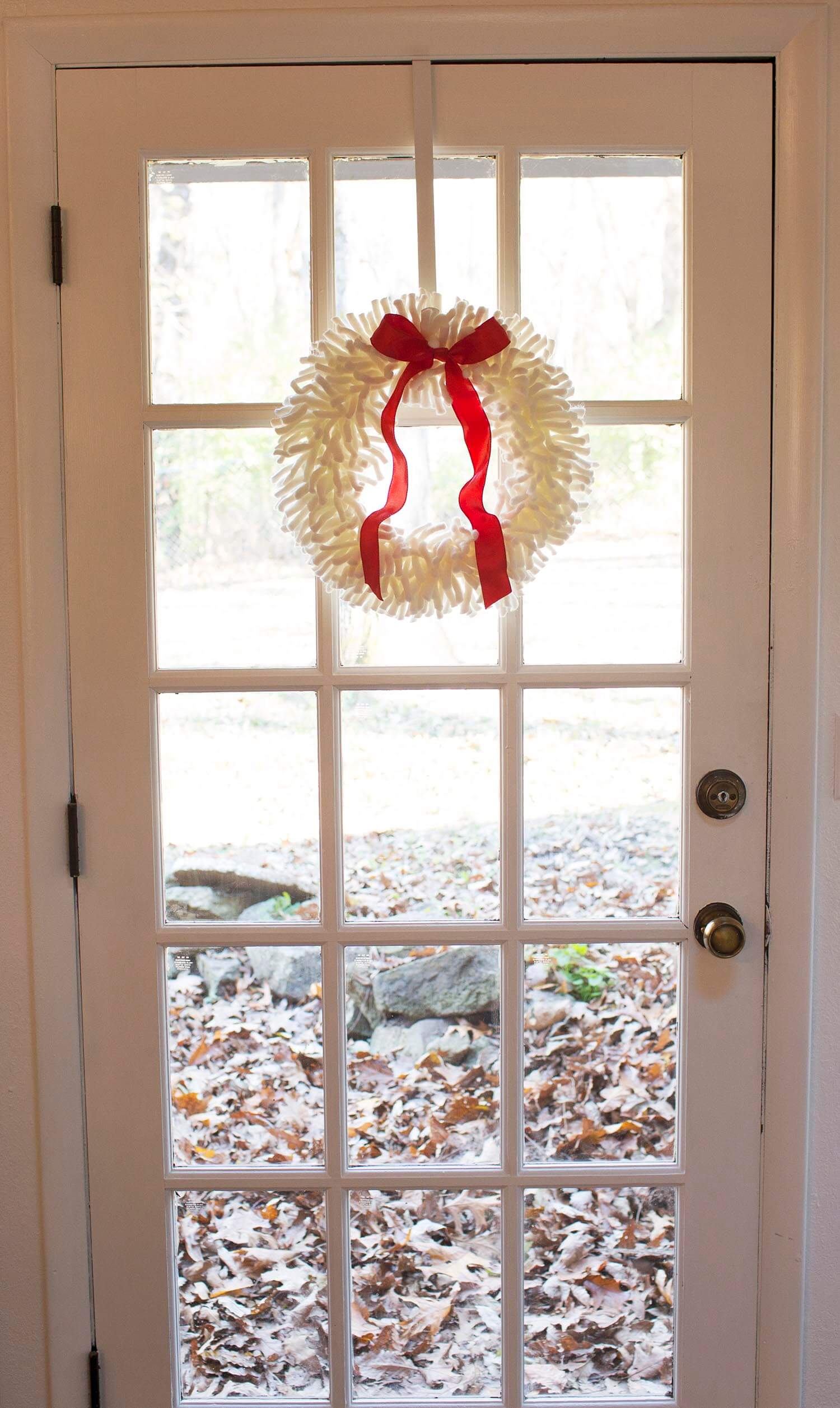 white yarn wreath with red ribbon hanging on door