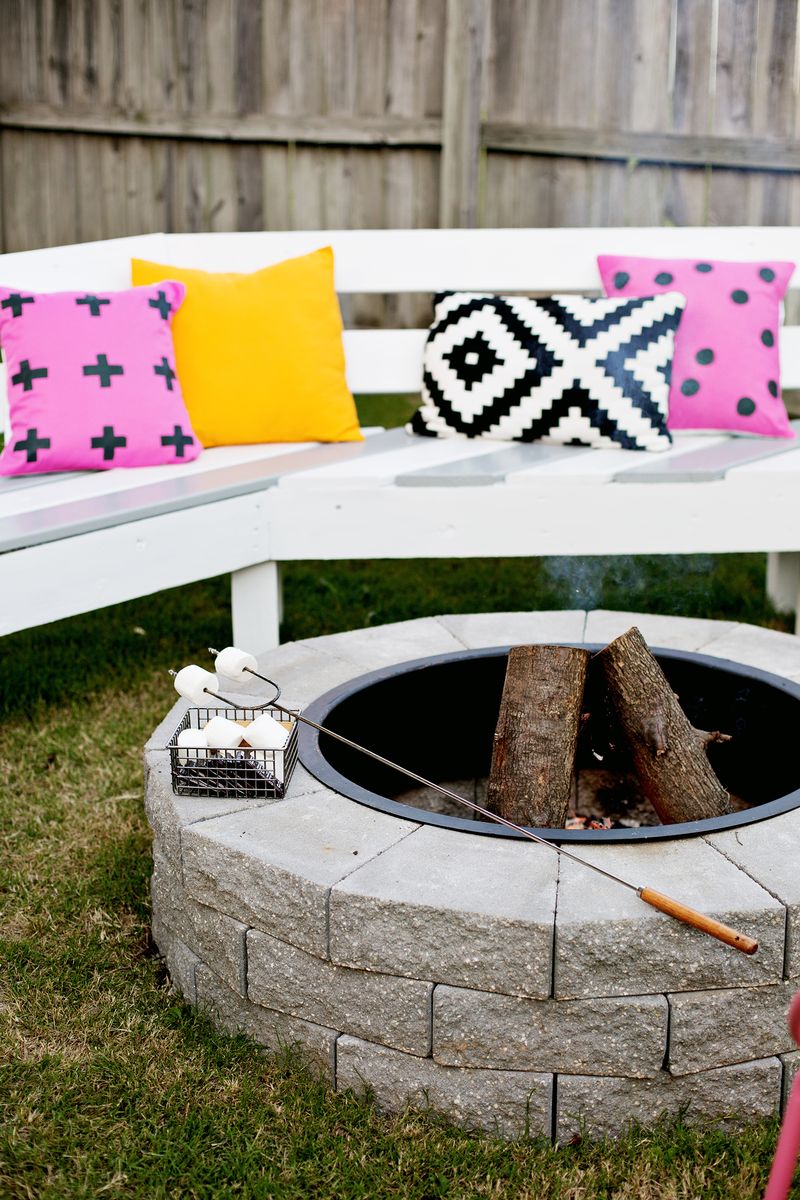 Fire pit with logs in it and a basket of marshmallows and marshmallow skewer on it surrounded by bench with pillows