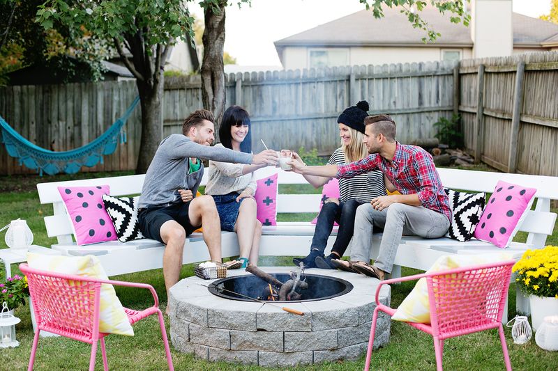 2 couples sitting on bench with pillows around the fire pit clinking their glasses together