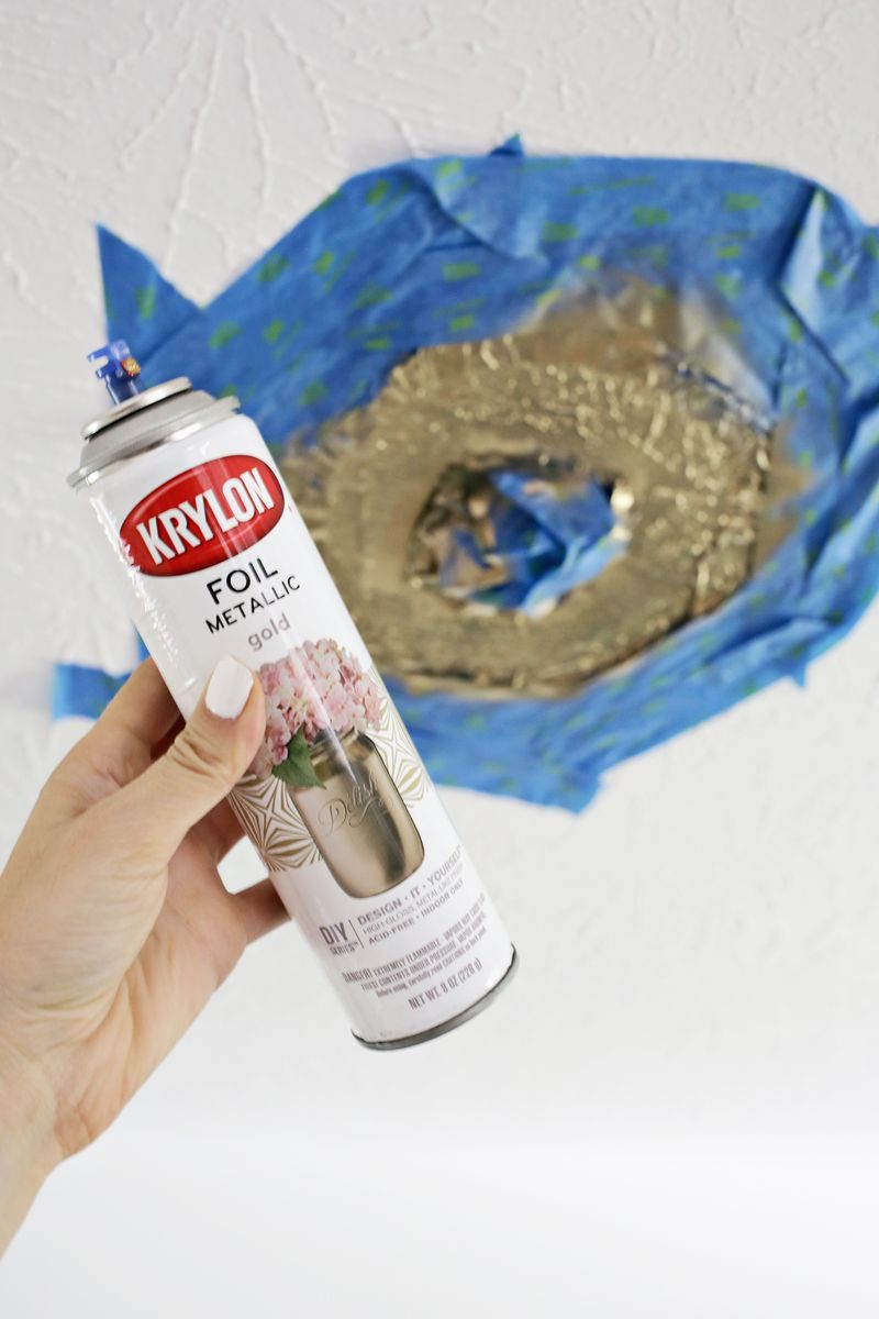 someone holding a can of foil metallic gold and a view of the ceiling with painter's tape around light fixture