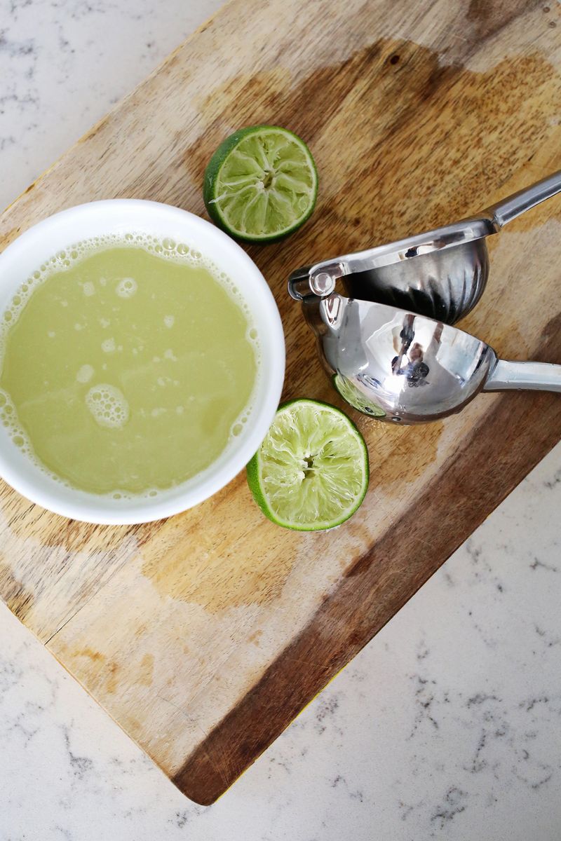 A bowl of lime juice with 2 half limes and a lime press on a cutting board