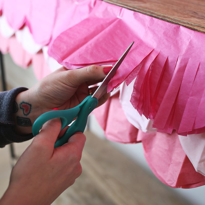 someone cutting a fancy scalloped border into the pink tablecloth with green scissors