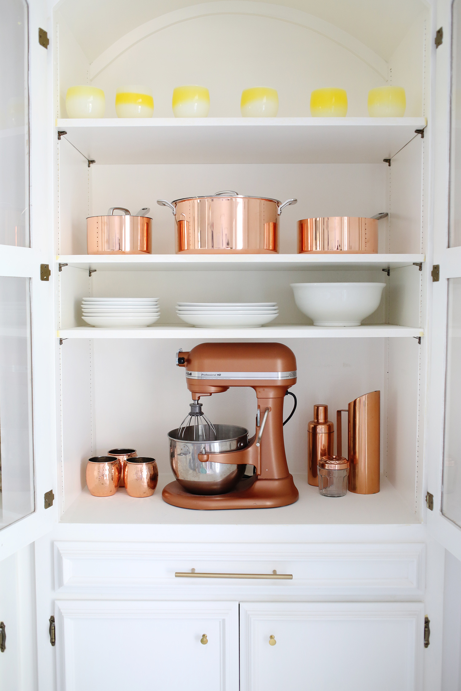 inside a cabinet with copper pots, a cooper blender, and white plates