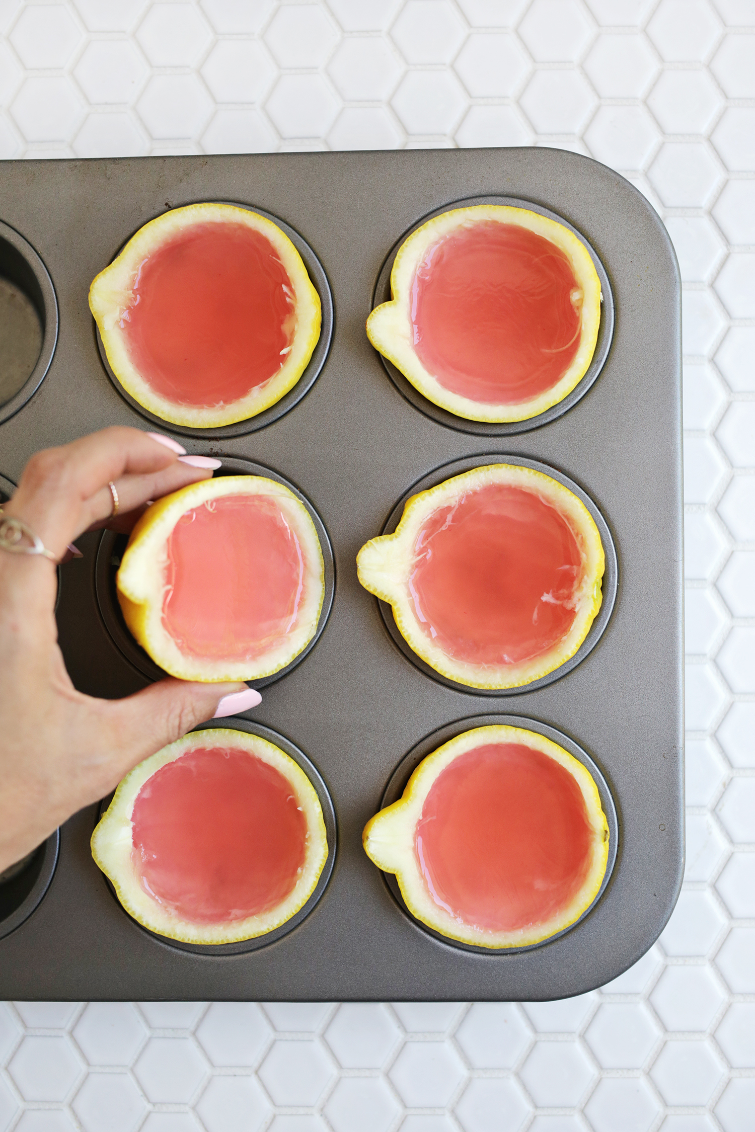 6 hollowed out lemon halves with pink lemonade in them in a muffin pan