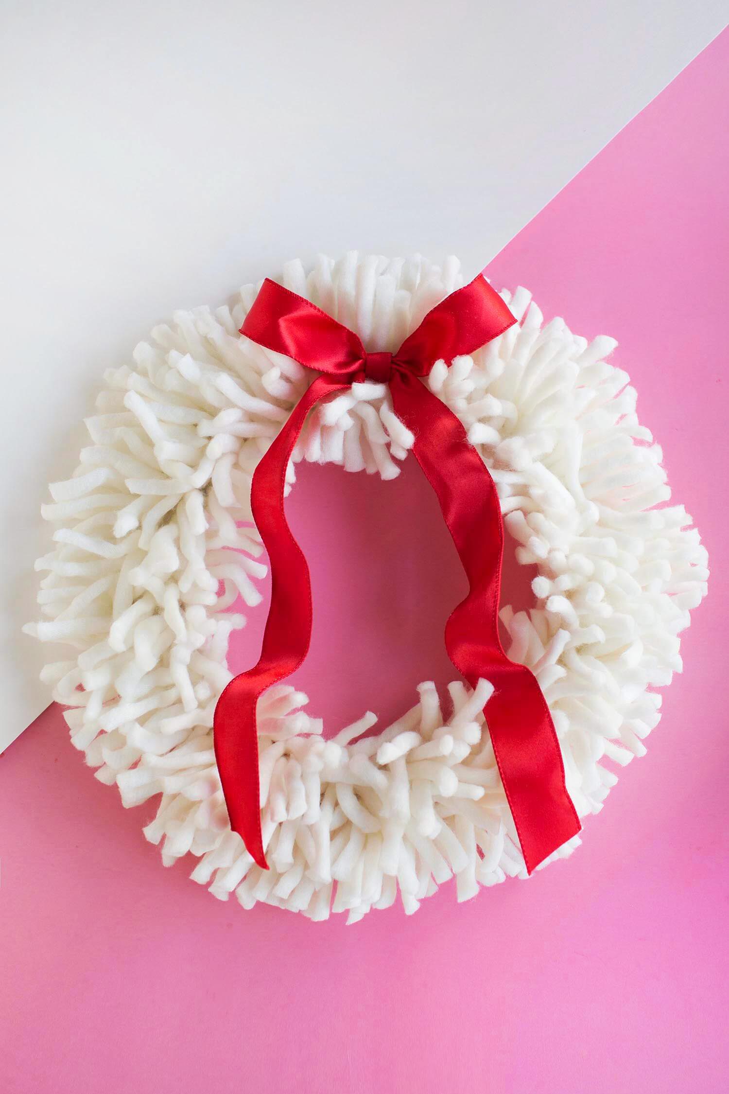 white yarn wreath with a red bow